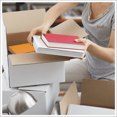 Person packing books into a cardboard box, ready to sell them online with WeBuyBooks