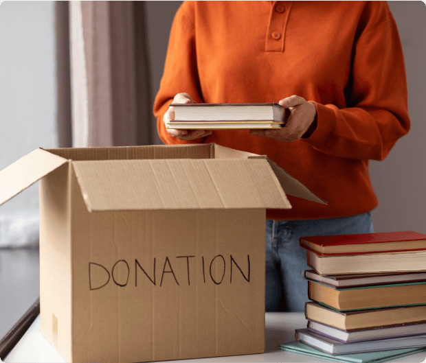 Person in orange jumper packing books into a cardboard box labelled 'Donation