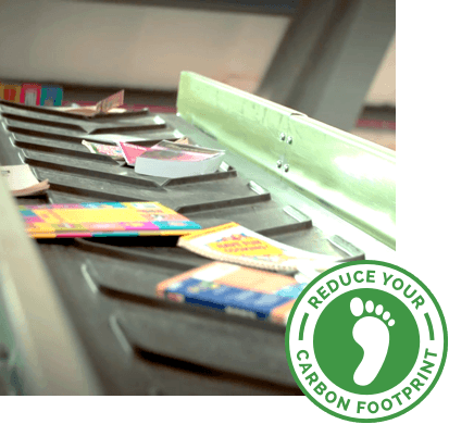 Books on a conveyor belt for recycling, with a Reduce Your Carbon Footprint badge