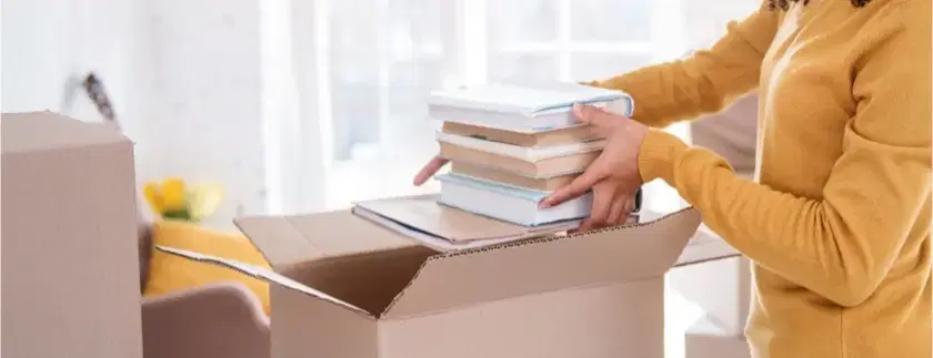 Woman packing a stack of books into a cardboard box ready to send to WeBuyBooks