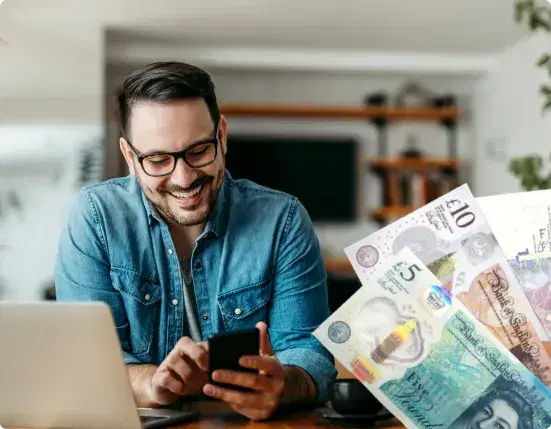 Man smiling at his phone by a laptop, with UK banknotes showing the payment he received for his books