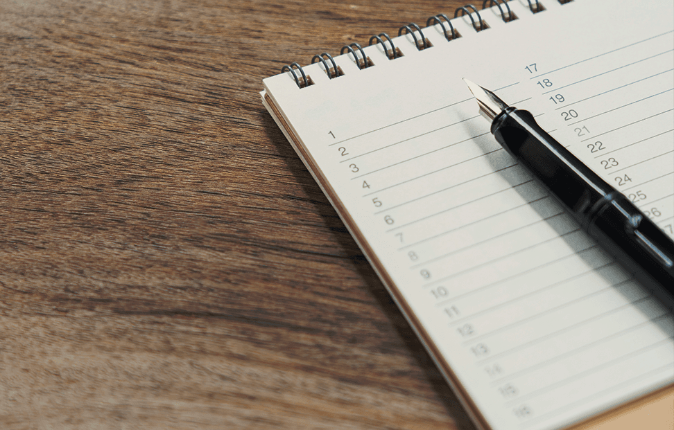 A fountain pen resting on a paper reading list on a wooden table.png
