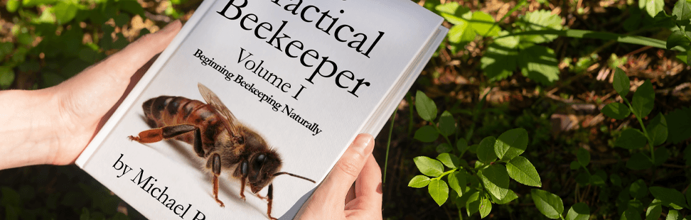 A person holding a copy of The Practical Beekeeper banner image.png