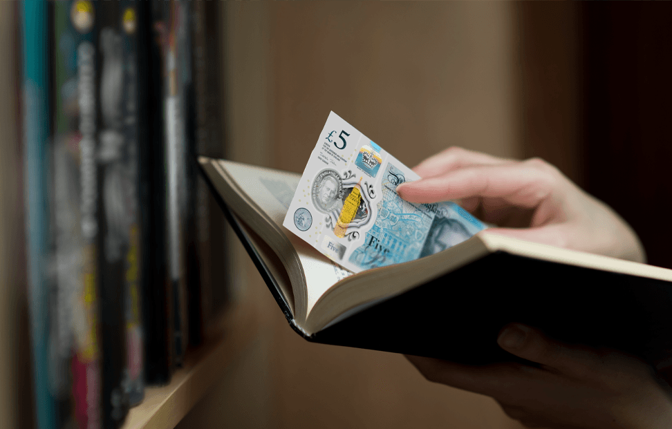 A person pulling a five pound note out of a language book.png