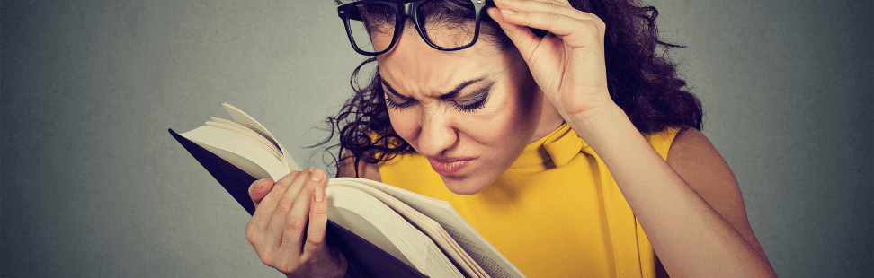 A woman wearing glasses pulling a funny face trying to read bad grammar in a book.png
