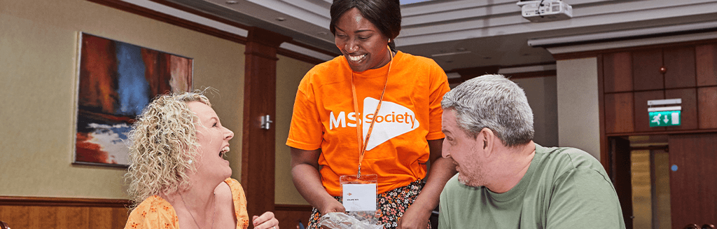 An MS Society volunteer laughing and talking to two people.png