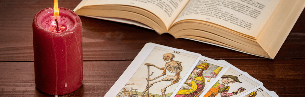 Fortune telling book on a table with some Tarot cards and a red candle.png