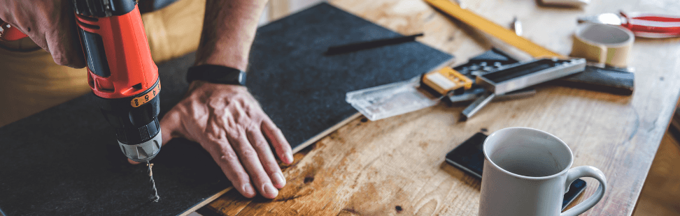 Man drilling a hole in a wooden board on a workbench.png