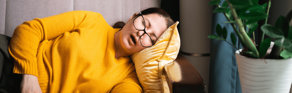 Woman in a yellow jumper asleep on a sofa with a book.png