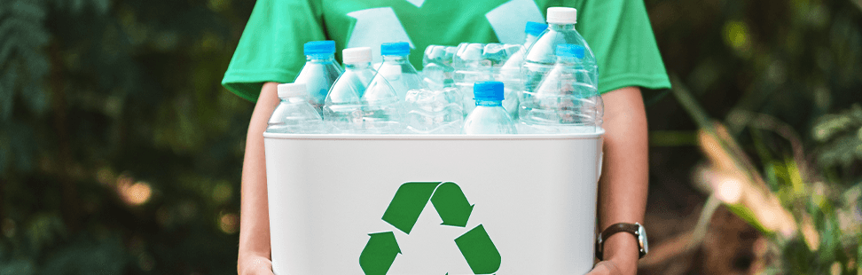 Person in a green recycling T-shirt holding a white recycling box filled with empty plastic bottles