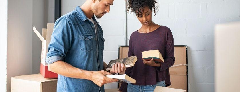 A man and a woman checking the condition of books beside stacked cardboard boxes