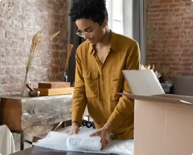 Woman wraps a book in bubble wrap before placing it into a cardboard box for posting